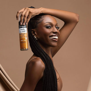 Woman with braided hair holding a bottle of hair product against a brown background