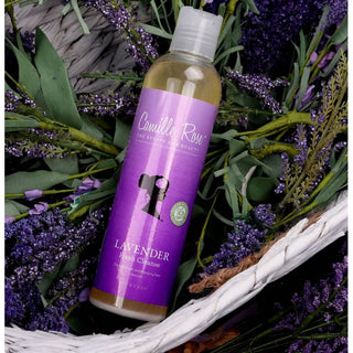 Bottle of Camille Rose Lavender Fresh Cleanse product surrounded by lavender flowers.