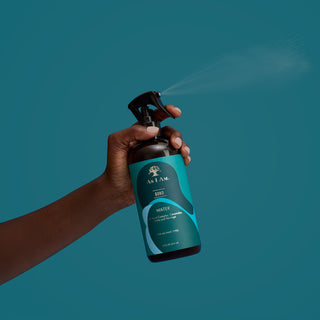 Hand holding a blue spray bottle with a brand logo against a teal background