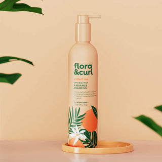 Flora & Curl shampoo bottle on a beige background with green leaves.