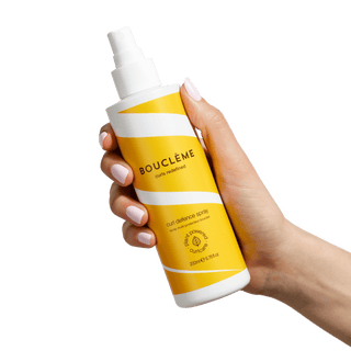 Hand holding a Bouleme hair spray bottle against a green background