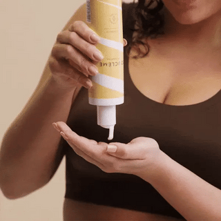 Person applying a tube of cream to their hand against a neutral background