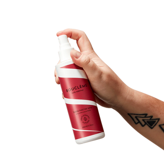 Hand holding a red and white spray bottle labeled 'Bouclème' against a white background