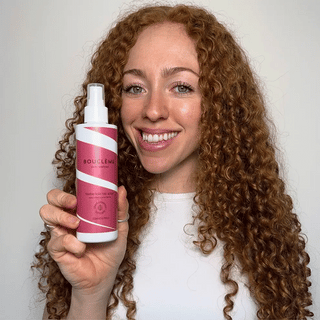 Woman holding a Boucleme hair product bottle with a plain background