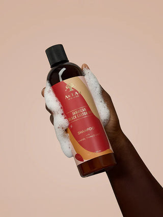 Hand holding a bottle of Jamaican Black Castor Oil Shampoo with a beige background