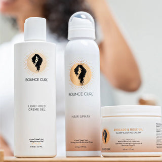 Bounce Curl hair care products including a bottle of light hold crème gel, a can of hair spray, and a jar of avocado and rose oil cream.
