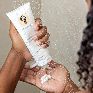 Person holding a tube of Bounce Curl hair product with visible cream on palm against a neutral background