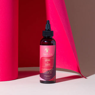 Bottle of 'Long & Luxe' hair oil with a red label against a pink and brown background