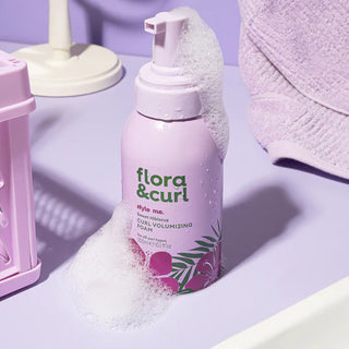 Flora & Curl volumizing foam bottle on a purple surface with bath products.