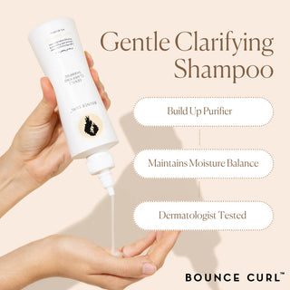 Bottle of Gentle Clarifying Shampoo being held with product being dispensed, on a beige background.