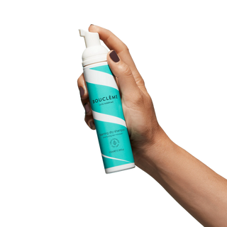 Hand holding a Boucleme dry shampoo can on a white background