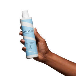 Hand holding a Boucleème hair care product against a white background