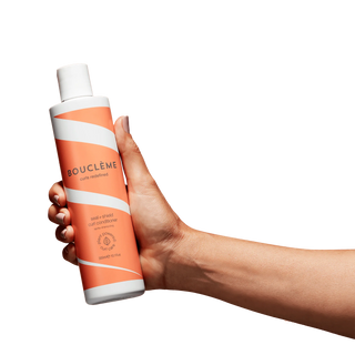 Hand holding a bottle of Bouclème conditioner against a white background