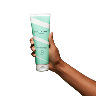 Hand holding a Green and white shampoo tube with 'Bouclème' branding on a white background