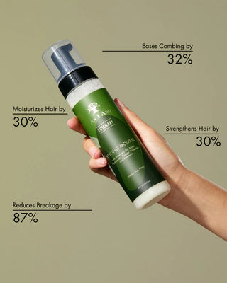 Hand holding a green hair product bottle with text on benefits against a beige background