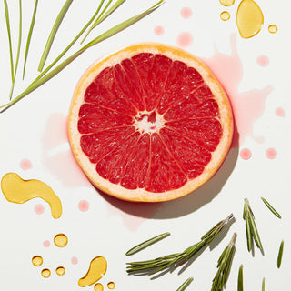 Half of a red grapefruit with green leaves and yellow droplets on a light background