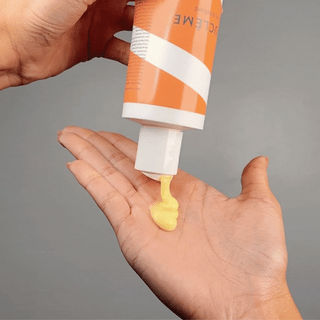 Hand holding an open tube of Vaseline with a small amount of yellow jelly on the palm against a gray background