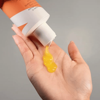 Hand holding a bottle with yellow gel dripping onto a gray background. Boucleme hair care product bottle on a white background