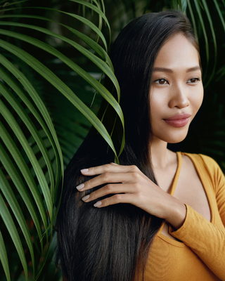 Asian woman with long dark straight hair holding a leafy plant