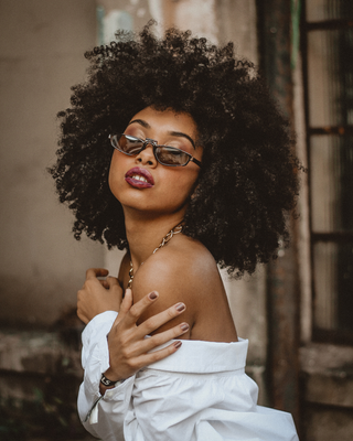 Woman with an afro wearing sunglasses and a white top in a blurred indoor setting