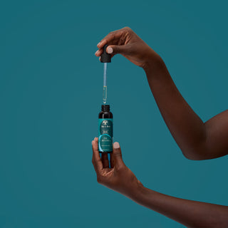 Hand holding a bottle with a dropper against a teal background