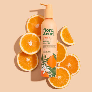 flora & curl shampoo bottle surrounded by sliced oranges on a beige background