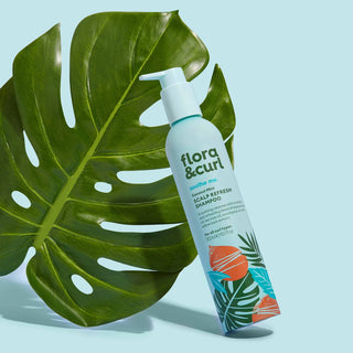 flora & curl shampoo bottle with a large green leaf on a light blue background