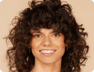 Woman with curly hair smiling against a beige background