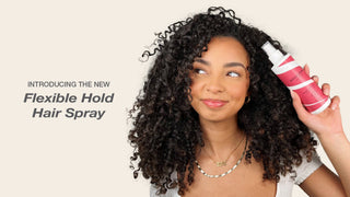 Woman with curly hair holding a can of hair spray against a beige background