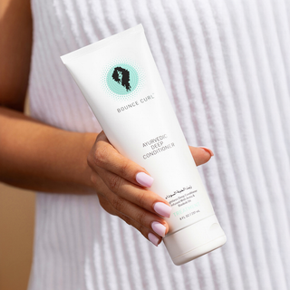 Hand holding a bottle of 'Bounce Curl' Ayurvedic Deep Conditioner against a neutral background