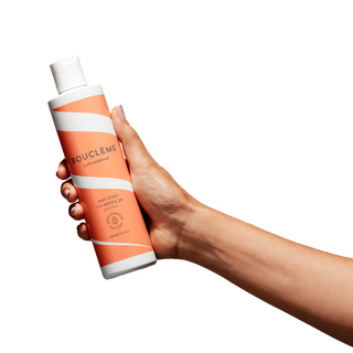 Hand holding a Boucleme hair care product on a white background