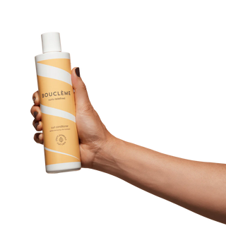 Hand holding a Boucleme hair conditioner bottle on a white background