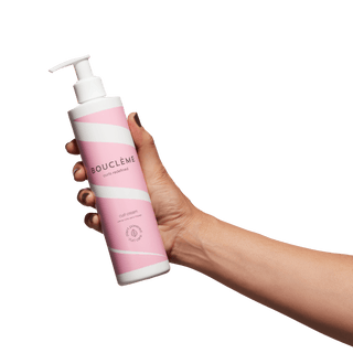 Hand holding a pink and white bottle labeled 'BOUCLEME' against a green background