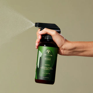 Hand holding a bottle of 'As I Am' Rosemary Water spray against a beige background
