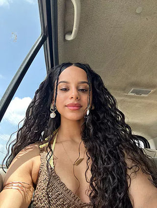 Woman with long, curly hair sitting inside a vehicle with a blue sky outside.